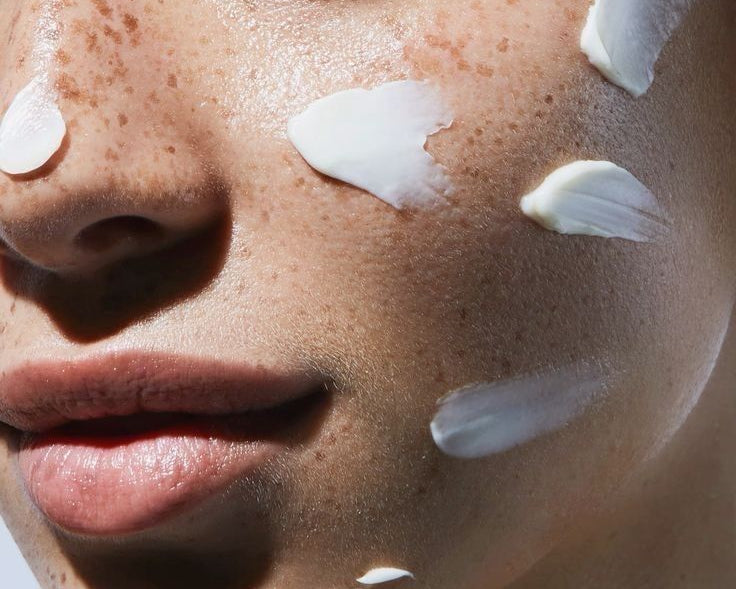 Close-up of a woman with dry skin applying multiple layers of moisturizing skincare, showing cream on cheek and chin