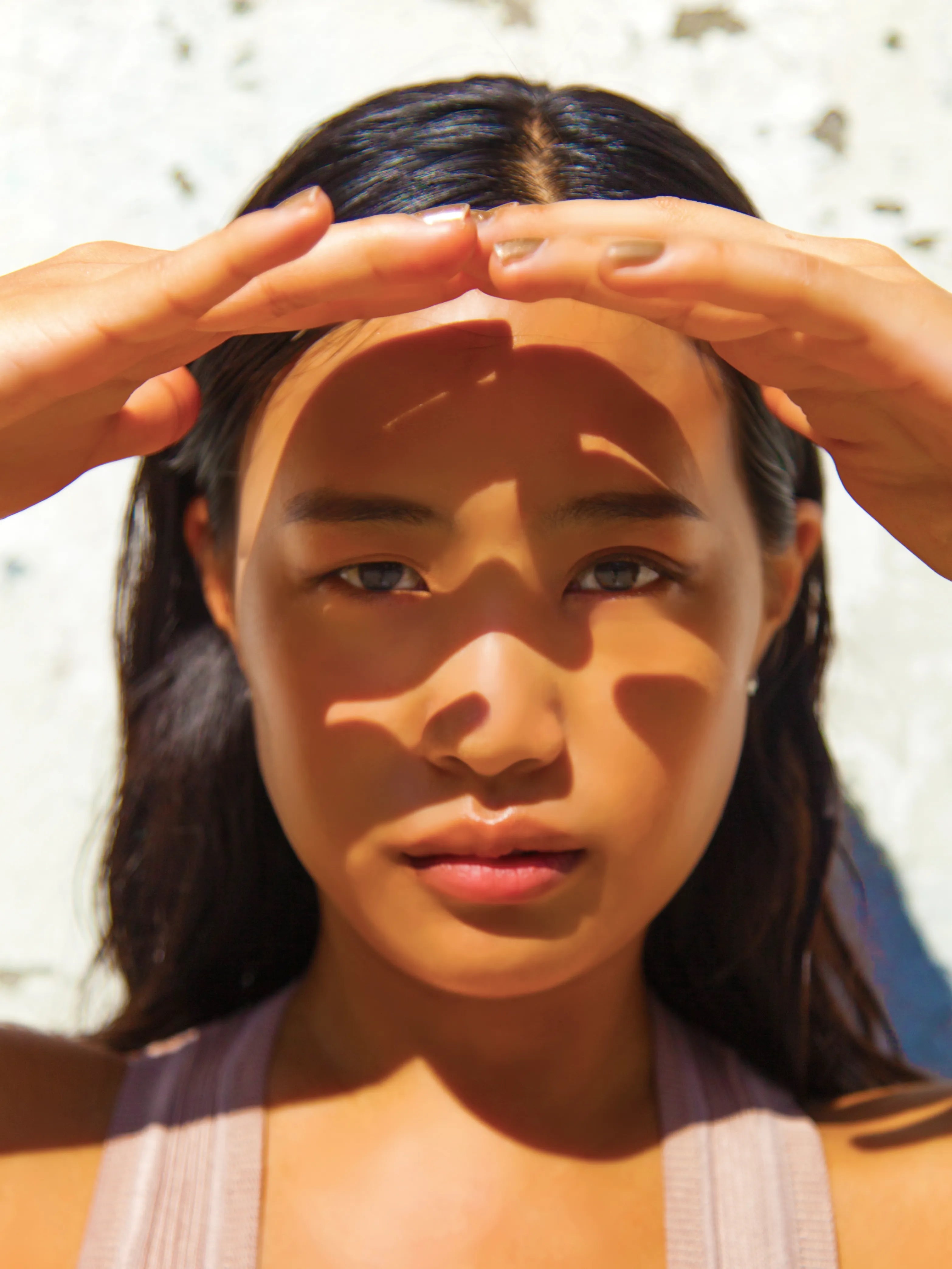 Close-up of a woman shielding her face from the sun, highlighting the effects of heat, humidity, and hormonal changes on skin health. Featured on Allana Davis Studio.